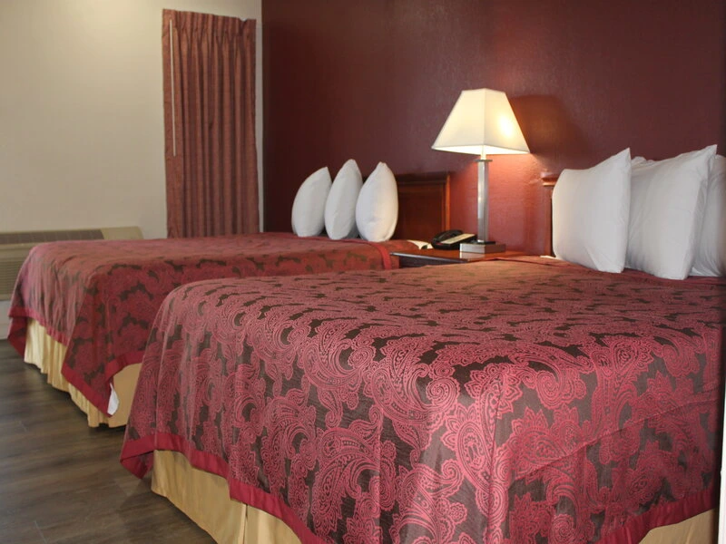 Two double beds with burgundy paisley bedspreads and white pillows in hotel room
