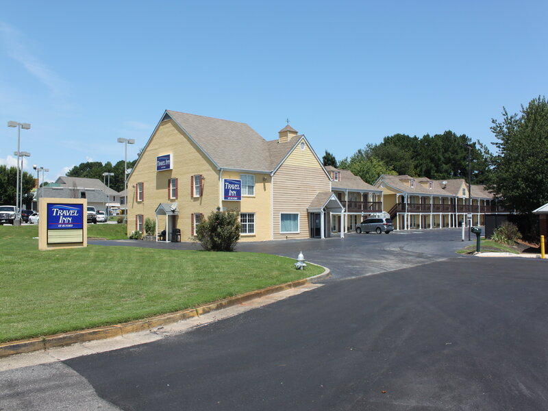 Yellow two-story exterior with guest rooms and parking area at Travel Inn of Buford