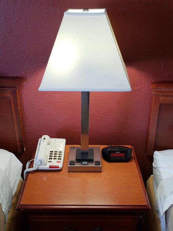 Nightstand with lamp, telephone, and alarm clock between beds at Travel Inn of Buford