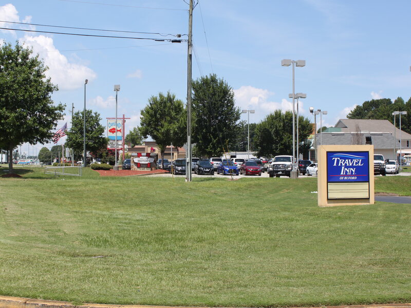 Blue and gold roadside sign with parking lot and green lawn at Travel Inn of Buford