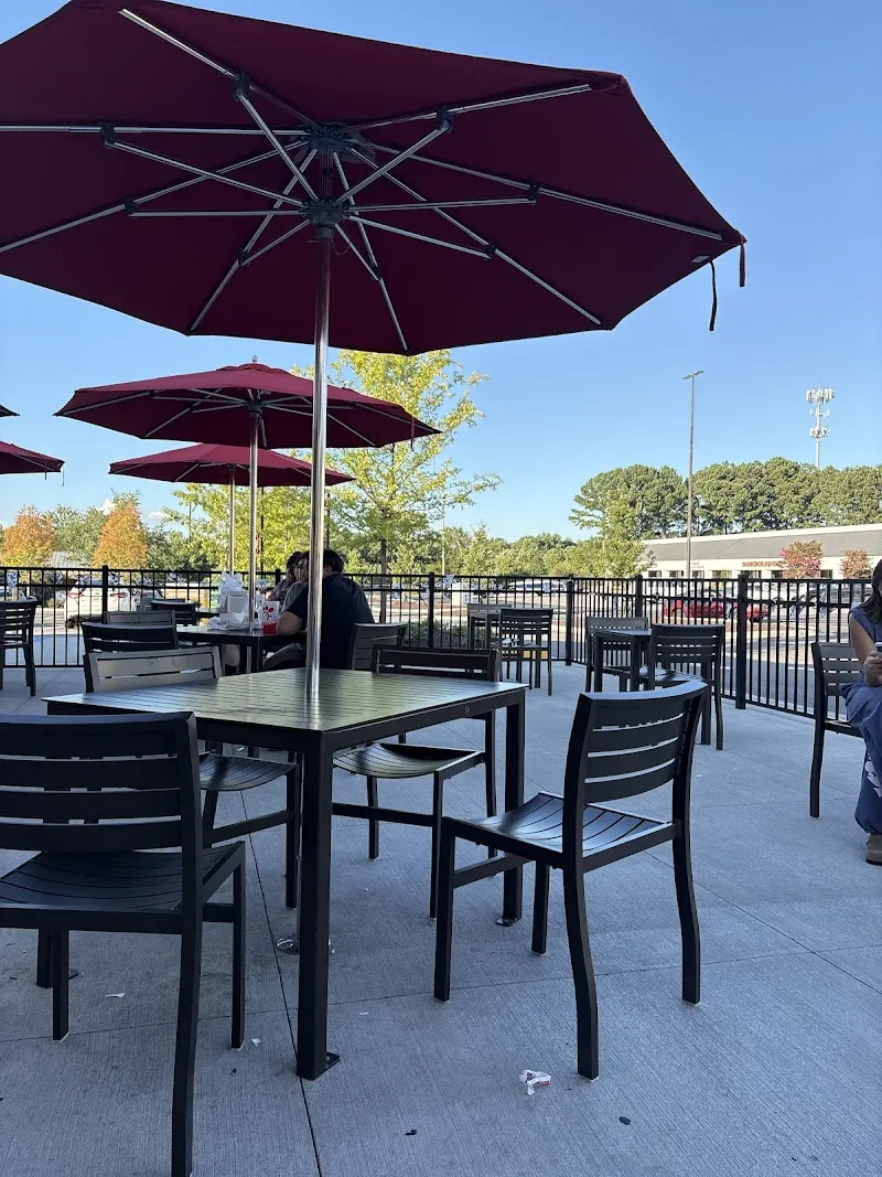 Outdoor patio seating with burgundy umbrellas and metal tables at Chick-fil-A